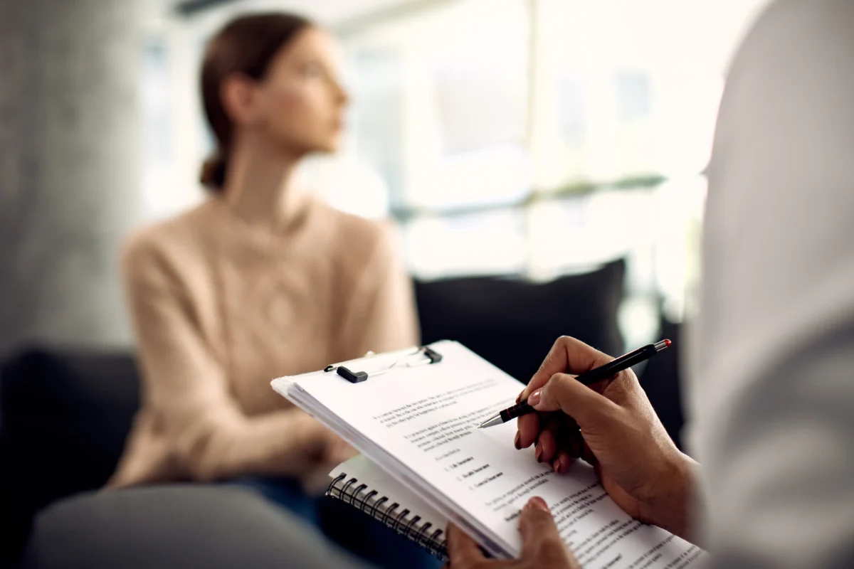 A psychologist takes notes on a clipboard during a patient consultation, representing the collaborative nature of psychotherapy for mental health support.
