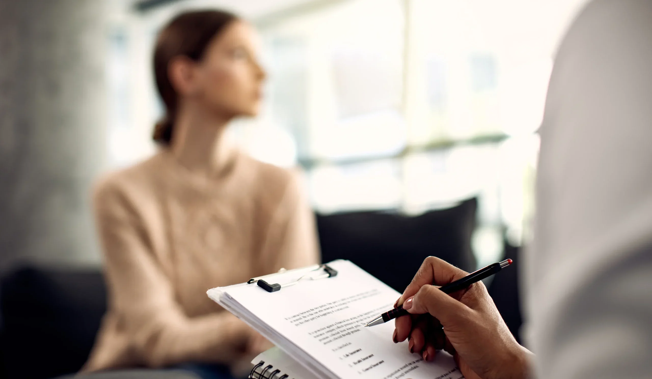 A psychologist takes notes on a clipboard during a patient consultation, representing the collaborative nature of psychotherapy for mental health support.