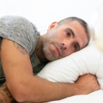 Man lying in bed with a thoughtful, unsettled expression, staring into the distance