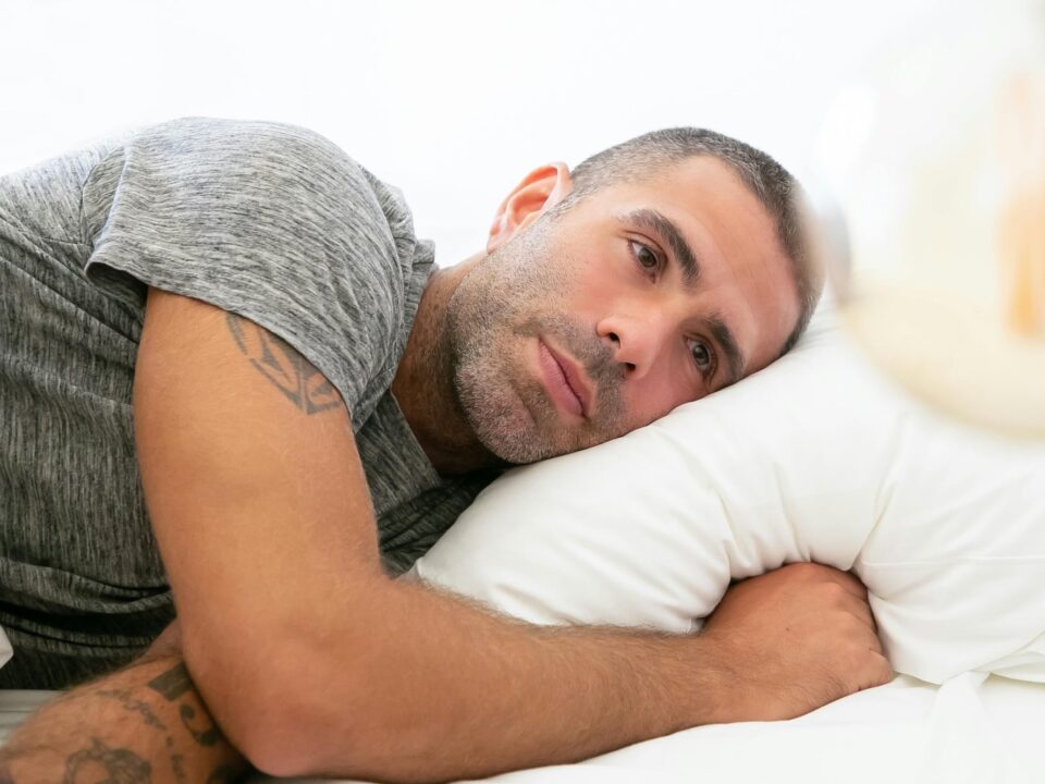 Man lying in bed with a thoughtful, unsettled expression, staring into the distance