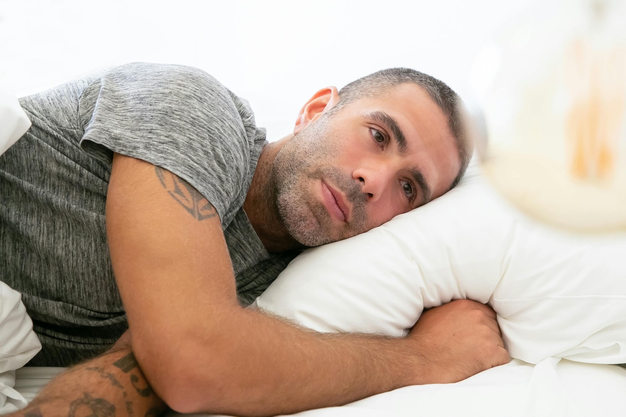 Man lying in bed with a thoughtful, unsettled expression, staring into the distance